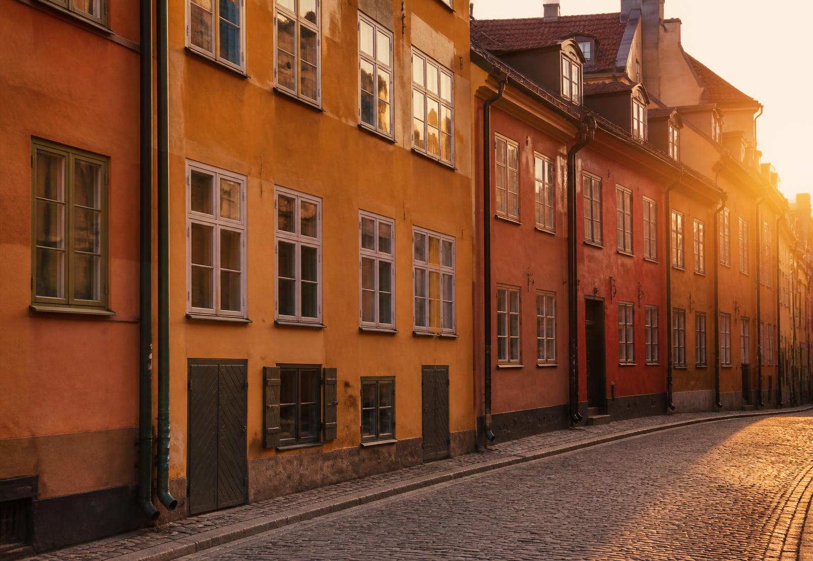 Ockrafärgade klassiska stockholmsfasader längs en kullerstensgata i kvällsljus